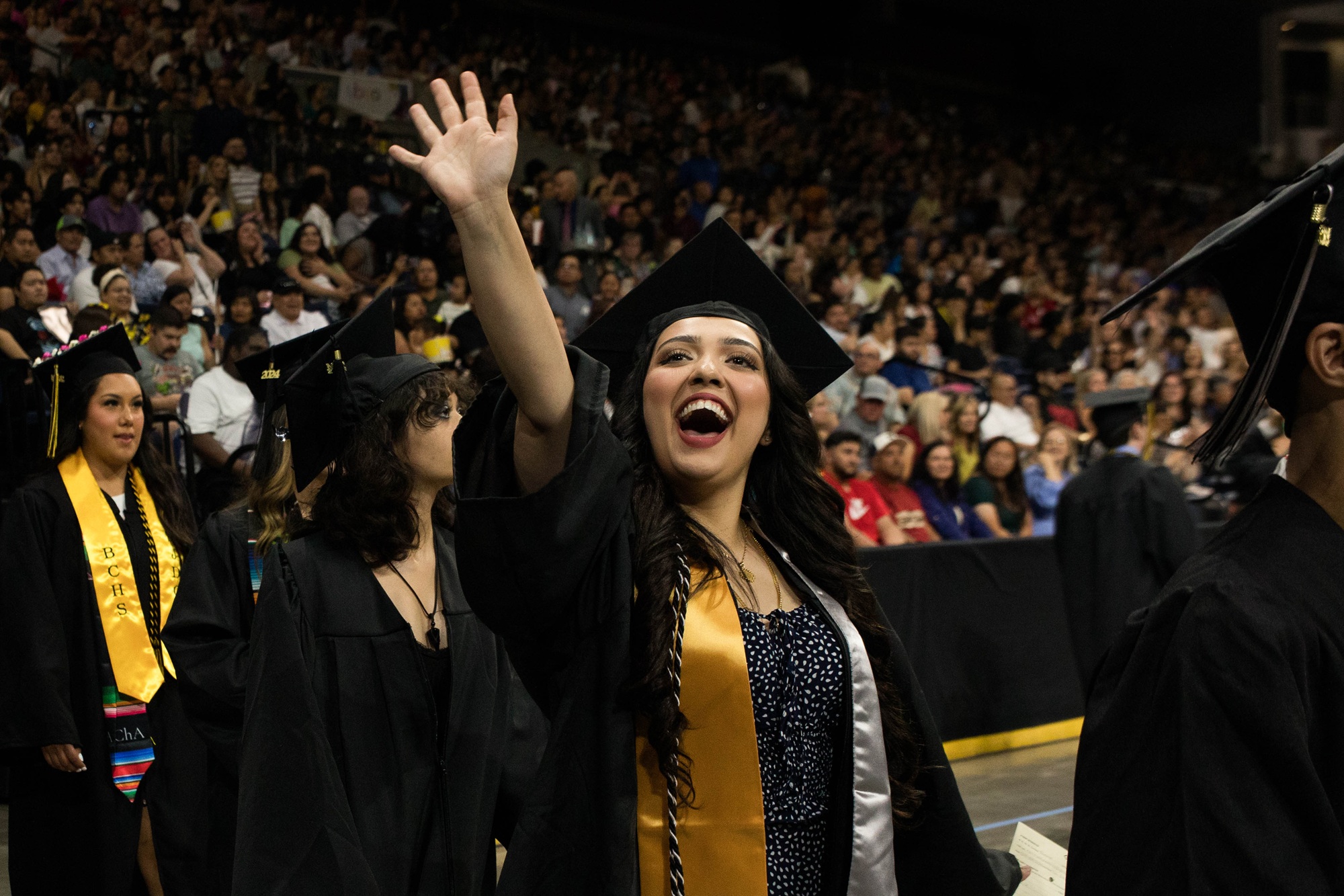 Photo of a Delta graduate waving to a family member at Commencement
