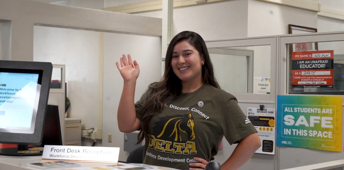 Video thumbnail showing a person with long dark hair smiling and waving hi. 