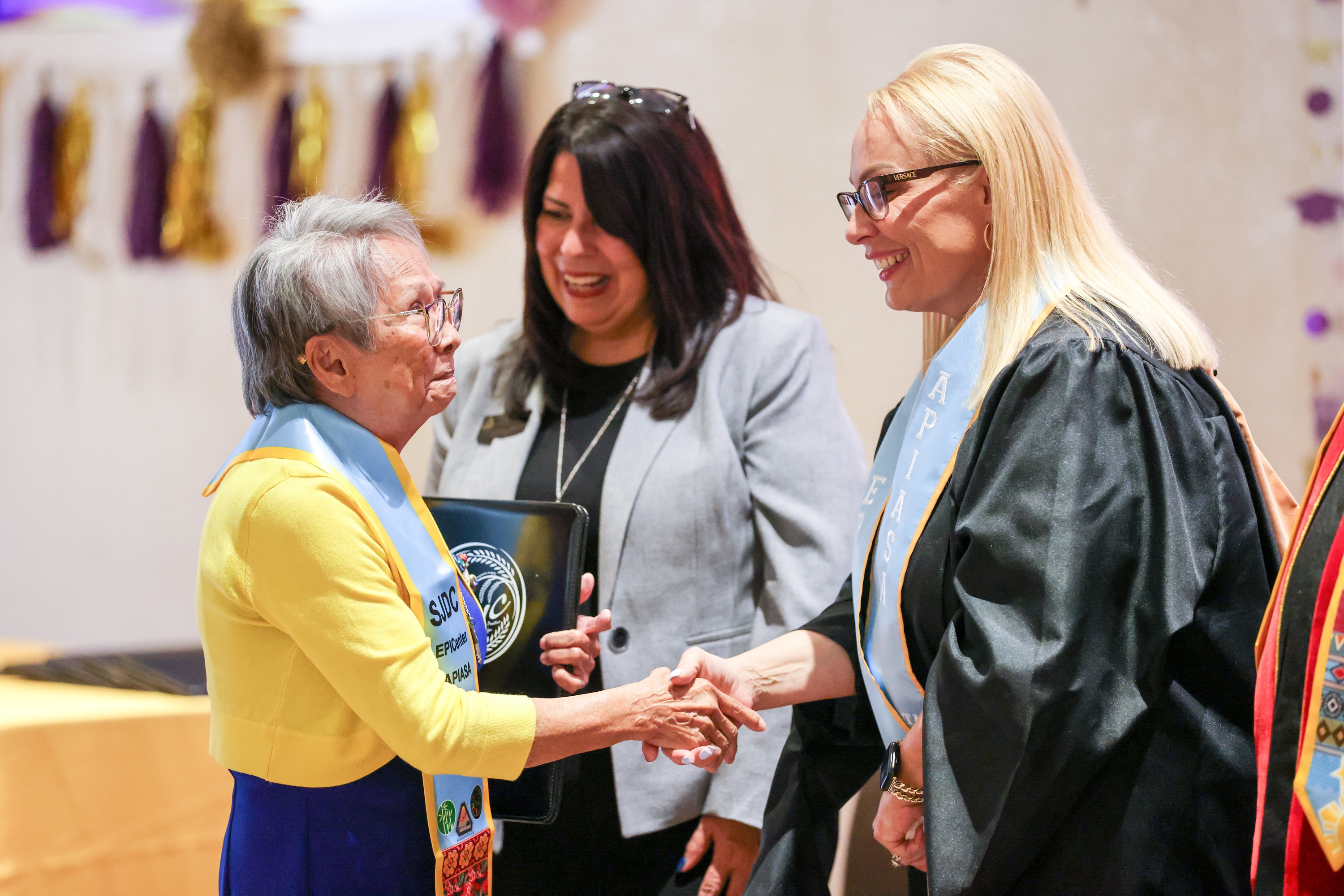 Photo of 80-year-old Veronica Smith being congratulated by College administrators