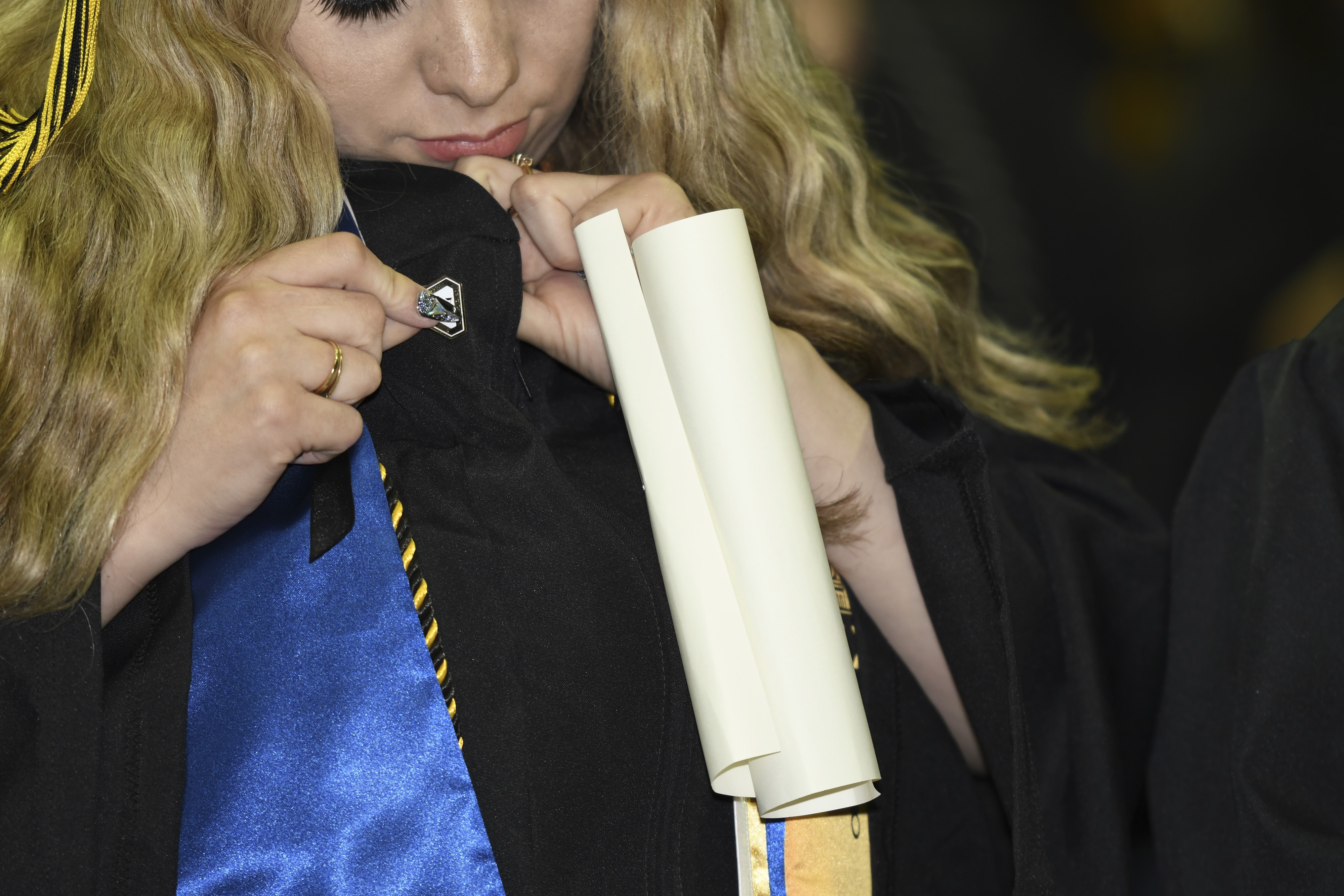 A new San Joaquin Delta College graduate puts on her alumni pin during the College's Commencement ceremony.