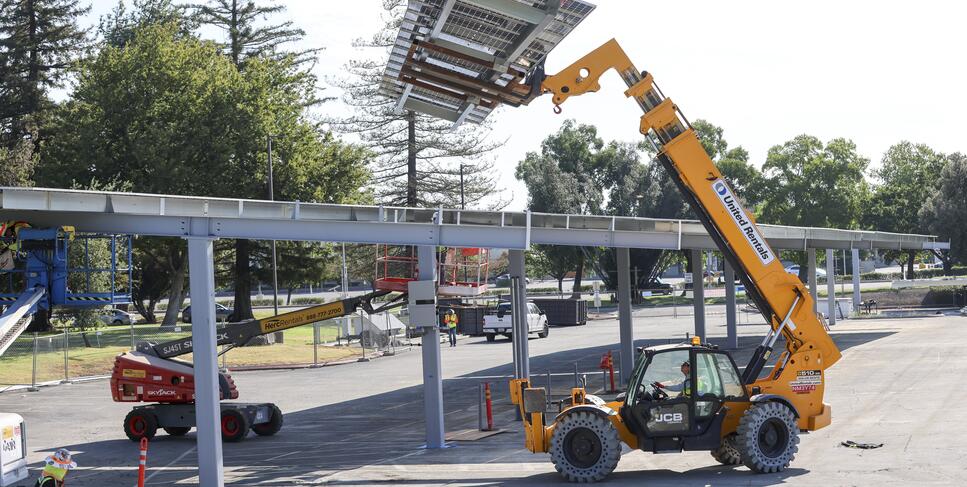 Photo of a loader hoisting solar panels at the L3 parking lot