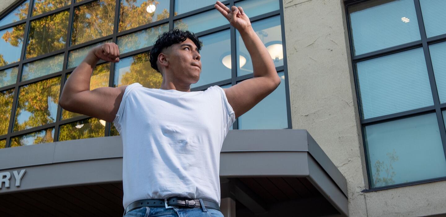 Photo of a student flexing his muscles in front of the library