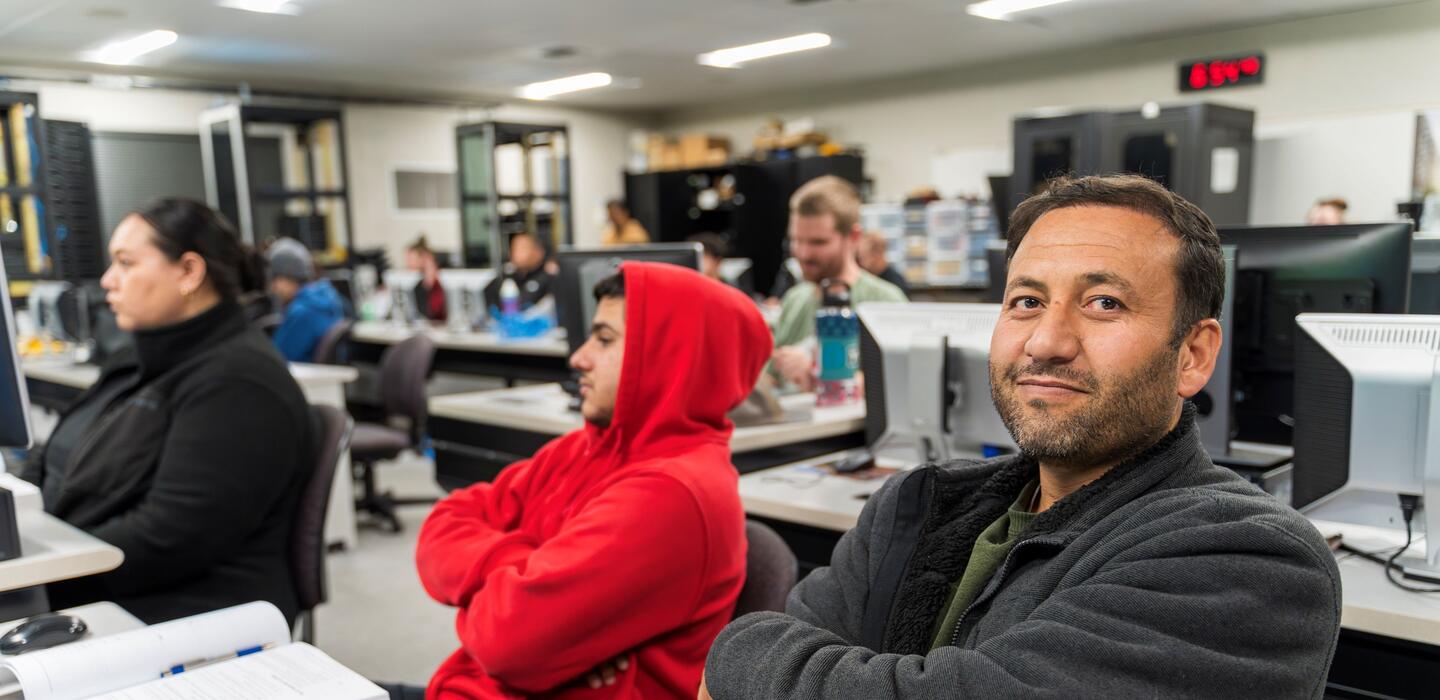A student sitting in a computer class with both arms crossed smiling. 