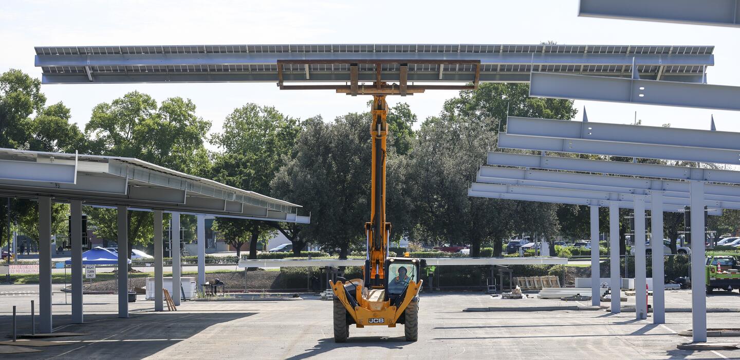 Photo of a loader hoisting solar panels in the L3 parking lot
