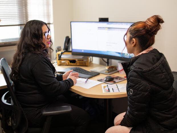 Staff member and student sitting together talking in front of computer