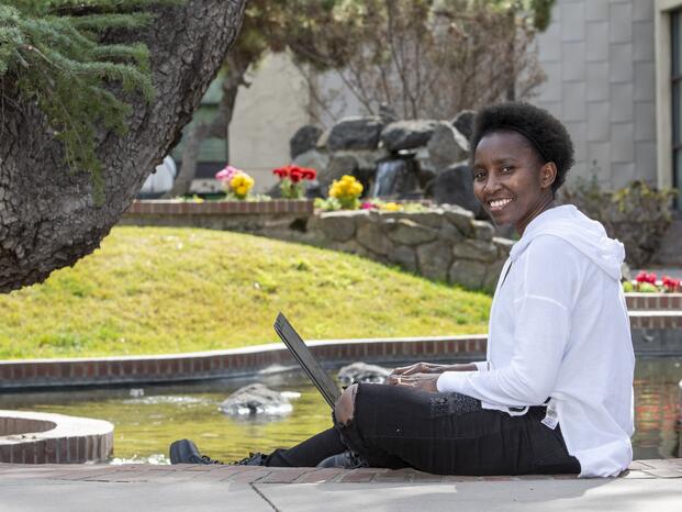 Student sitting near koi pond at Delta College posed and smiling while holding an open laptop