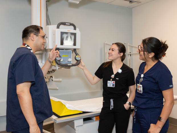 Three people in scrubs are examining a medical machine together, discussing its features and functionality.