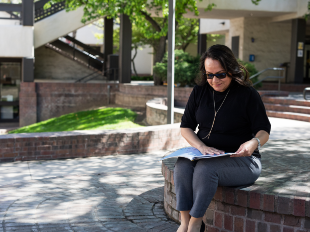A woman sits on a brick wall, reading a book, enjoying a peaceful moment outdoors.