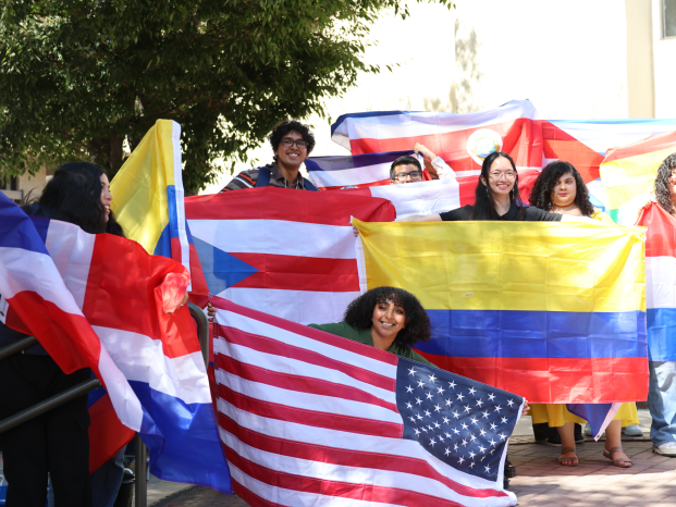 Group of diverse young people holding and waving various national flags outdoors on a sunny day, smiling happily.