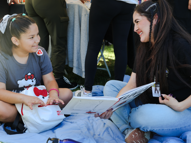 A woman and a girl sit together on the ground, sharing a moment of joy and connection.