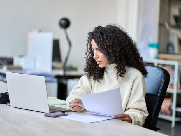 A woman sitting at a desk, focused on her laptop, with a cozy workspace around her.