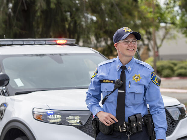 POST Academy student smiling in the distance standing in front of security vehicle