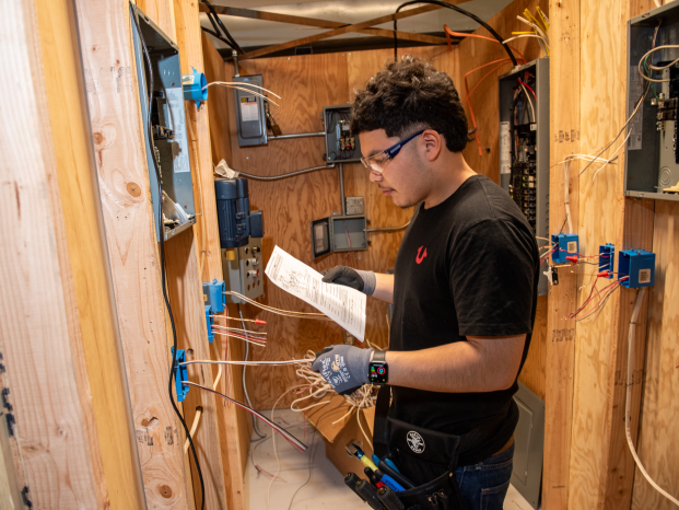A man in a black shirt is focused on repairing electrical equipment.