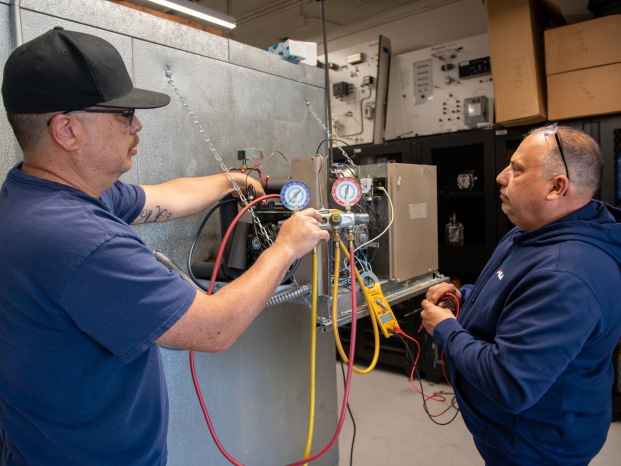 Two men collaborating on a machine in a factory setting, focused on their work and surrounded by industrial equipment.
