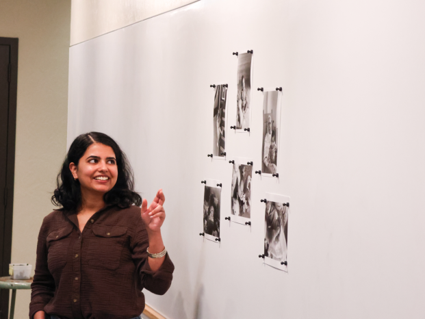 A female photography student proudly presents her work attached on a whiteboard in a classroom setting.