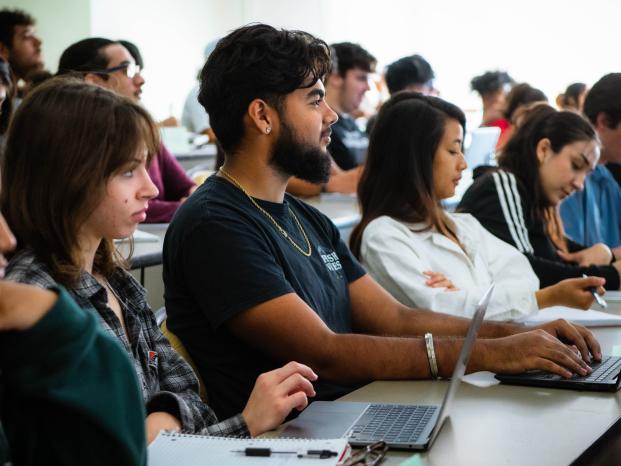 Students in a lecture hall attentively using laptops to take notes and engage with the lecture content.