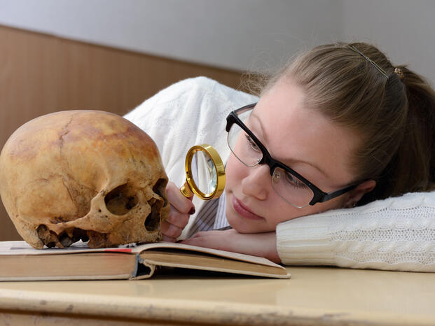 A girl looking at a skull with a lens magnifier