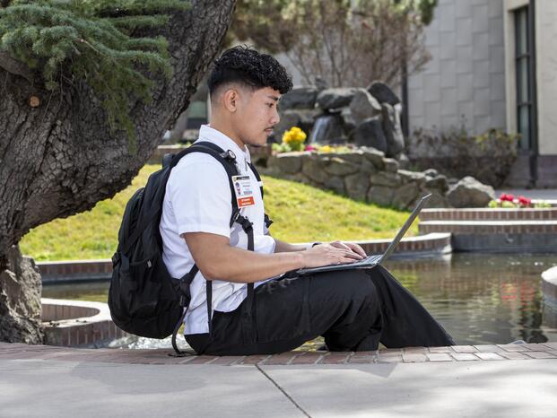 Student sitting near koi pond while using their laptop