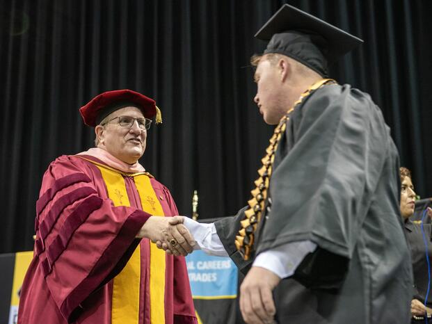Photo of a Board member shaking hands with a graduate at Commencement