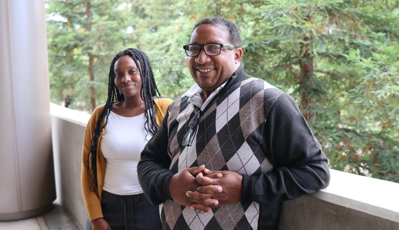 Two people standing next to each other smiling with tall green trees in the background