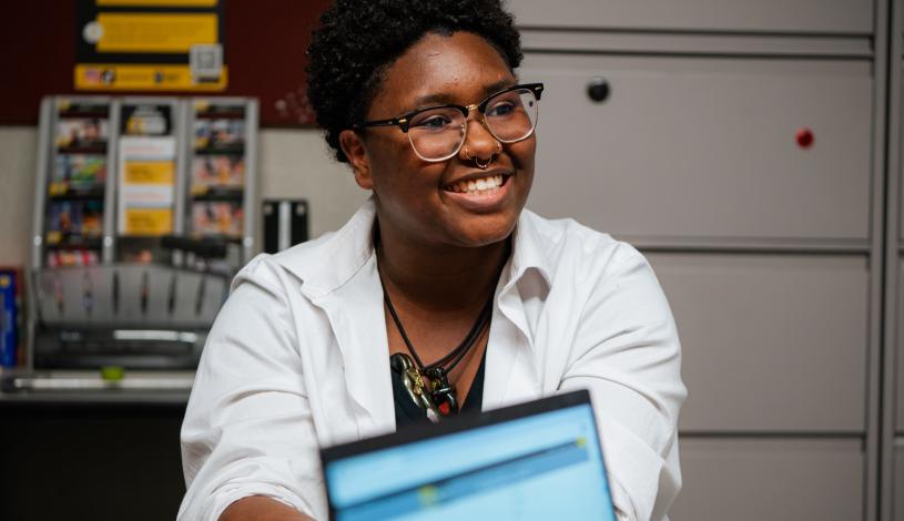 Student sitting in office behind laptop smiling