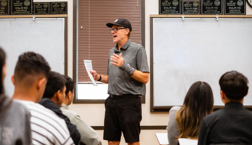 Professor standing at front of classroom lecturing to small classroom full of students