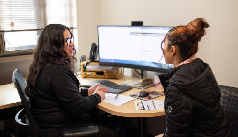 Staff member and student sitting together talking in front of computer