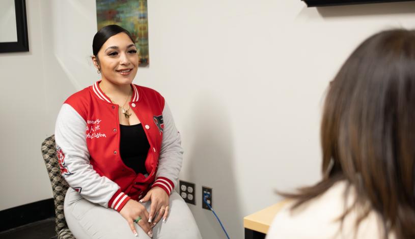 Student sitting in chair in an office talking to a counselor