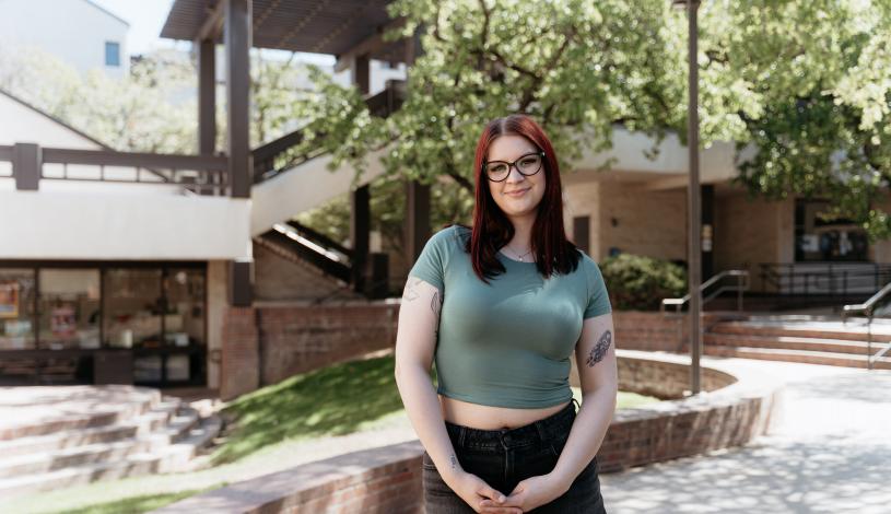 Student wearing green top standing in Quad Center of campus smiling
