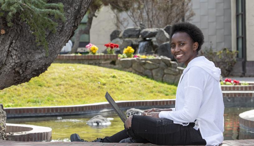 Student sitting near koi pond at Delta College posed and smiling while holding an open laptop
