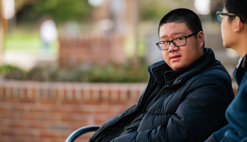 A student sits on a bench and talks to his friend