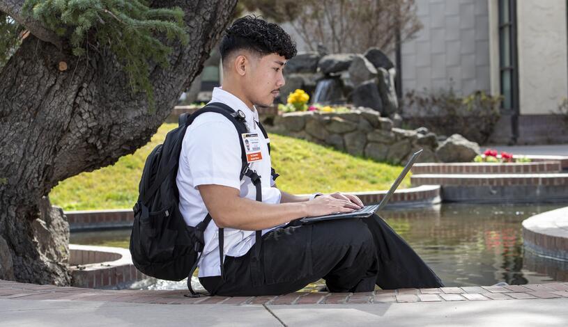 Photo of a student sitting by koi pond using laptop