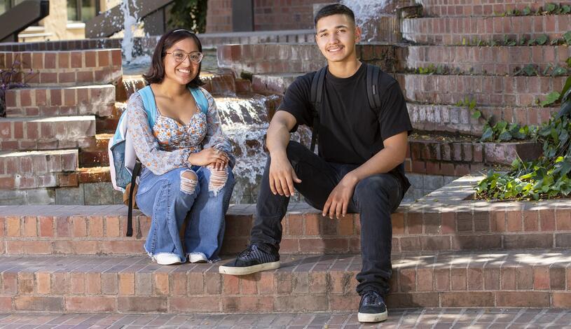 Two young students sit on the brick steps by the Budd fountain and smile