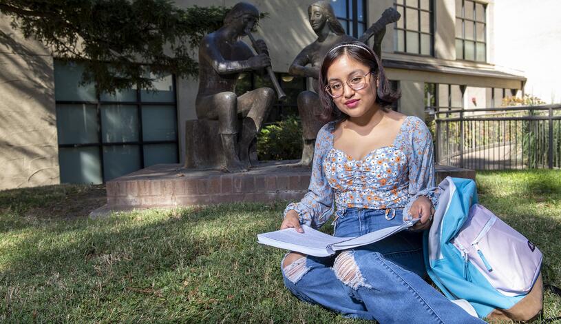 A student sits on the grass in front of the Goleman Library