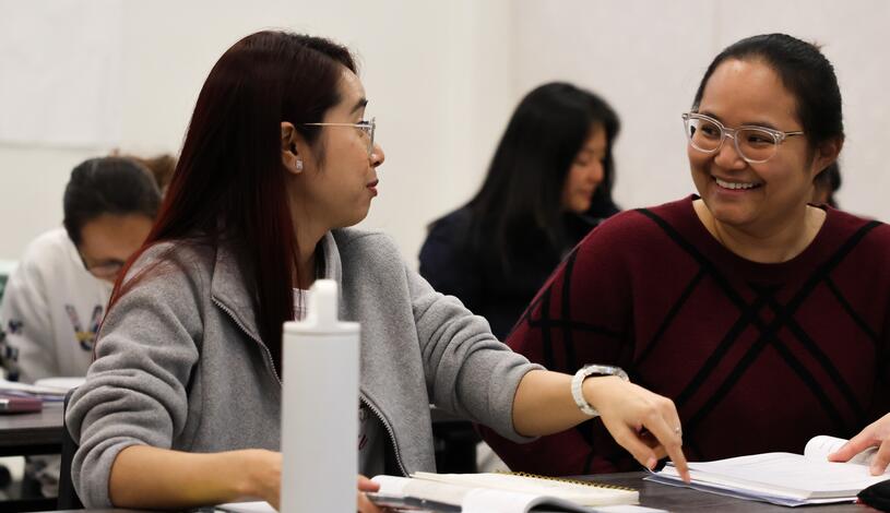 Photo of two ESL students talking and smiling in class.