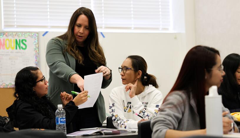 an instructor pointing at a group of students schoolwork in a classroom