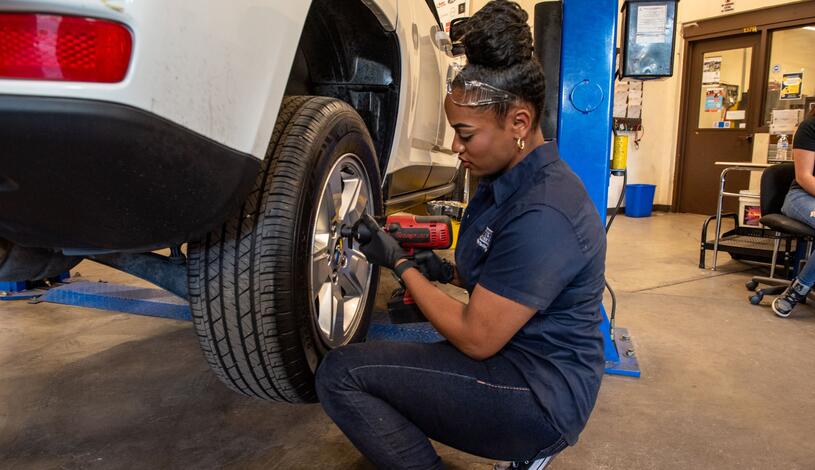 A student holding a tool and working on a tire