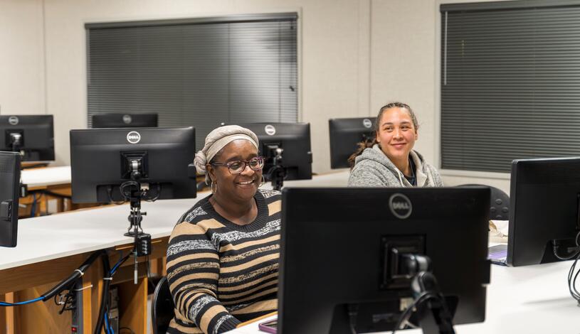 Two students sitting down in front of a monitor.