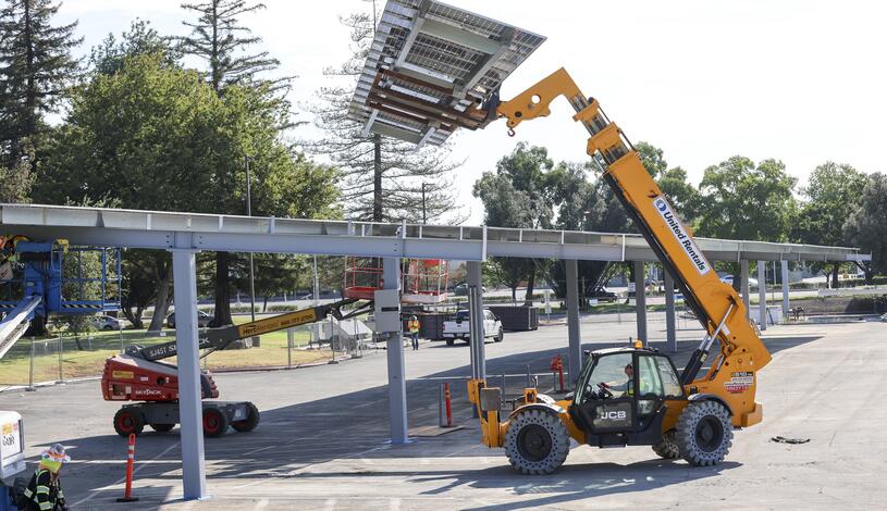 Photo of a loader hoisting solar panels at the L3 parking lot