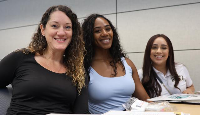 Three women sitting behind a desk with papers on the desk and all smiling