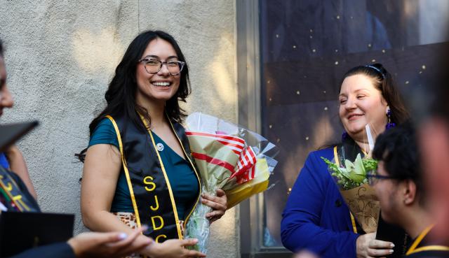 Person holding flowers wearing an SJDC stole smiling in the distance