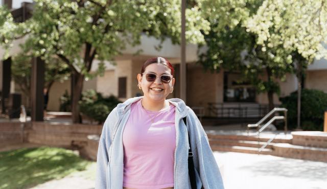 Female student standing in quad center smiling wearing sunglasses
