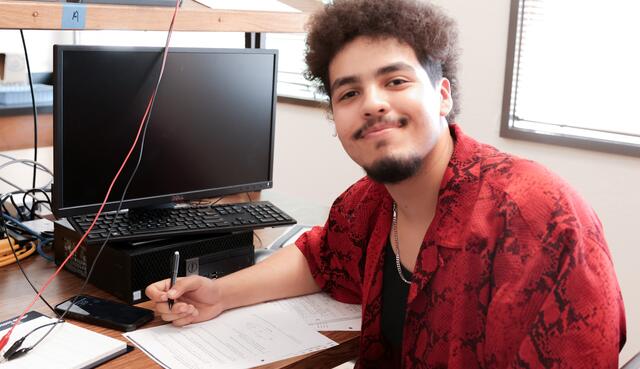 A student sits at his work station and smiles for the camera.