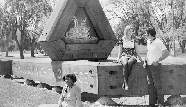Black and white photo of students hanging out near the Delta logo sign on campus