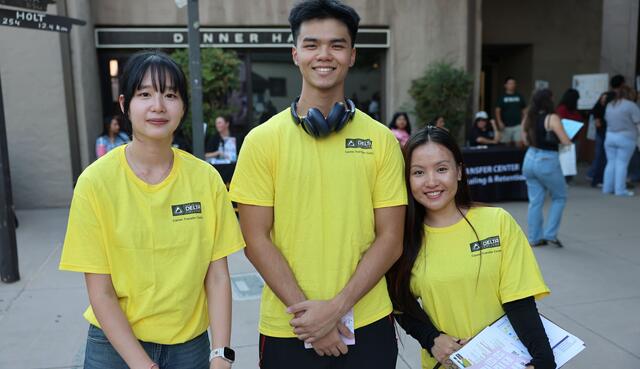 Three students wearing yellow t-shirts outdoors smiling.