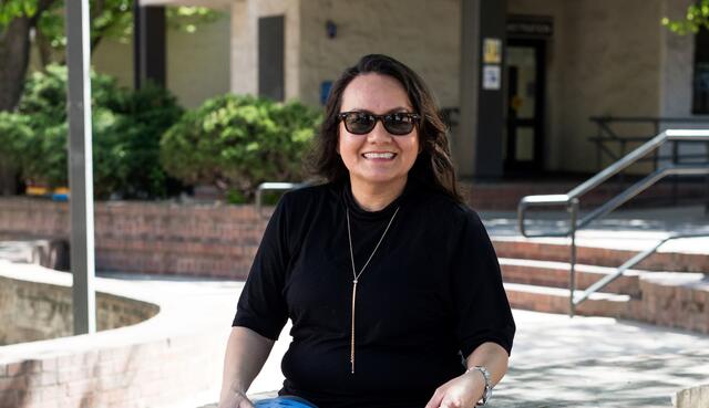 A student sitting down holding a book and smiling. 