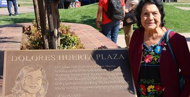 Dolores Huerta stands next to a plaque in her honor at Dolores Huerta Plaza