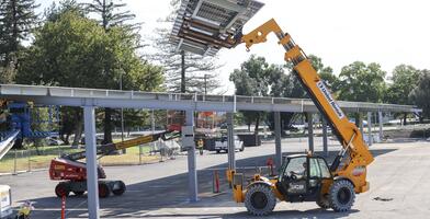 Photo of a loader hoisting solar panels at the L3 parking lot