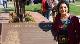 Dolores Huerta stands next to a plaque in her honor at Dolores Huerta Plaza