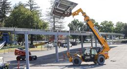 Photo of a loader hoisting solar panels at the L3 parking lot